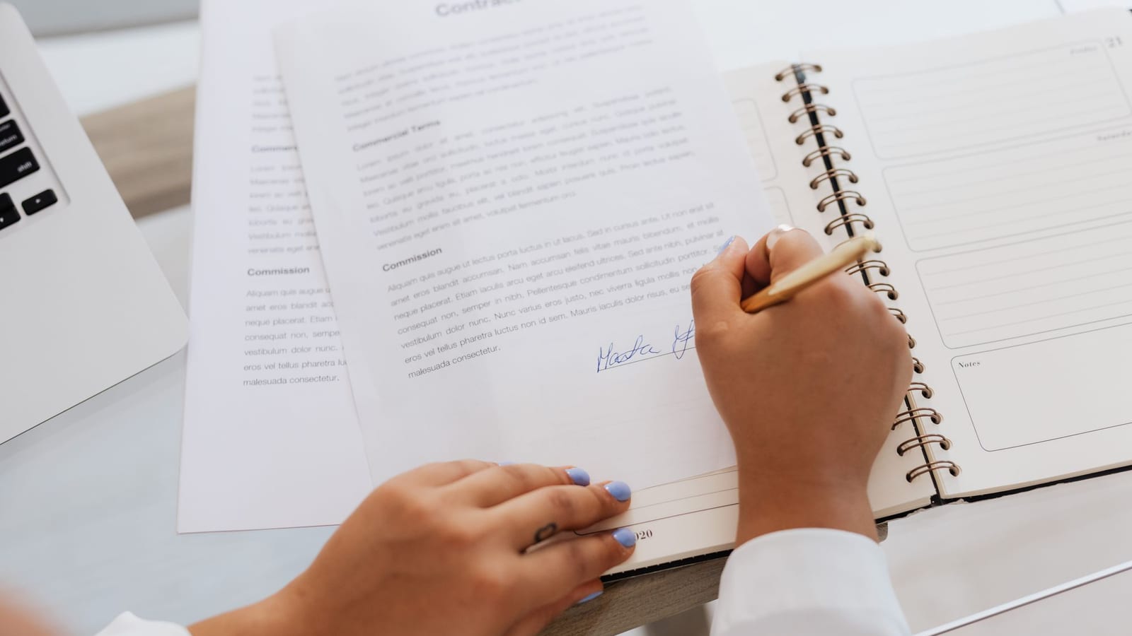 Main signant un contrat à côté d’un ordinateur portable